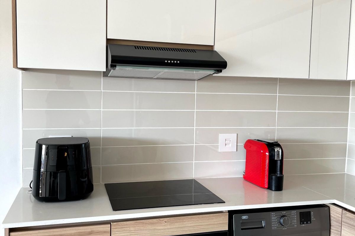 Modern kitchen featuring sleek white and wood-grain cabinetry, stone countertops, a tiled backsplash, and integrated appliances including an oven, hob, and washing machine.