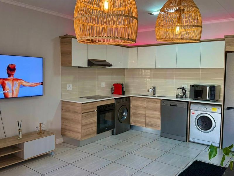 Modern open-plan kitchen featuring sleek wood-finish cabinetry, integrated appliances, tiled backsplash, and contemporary lighting, seamlessly connected to the living area.
