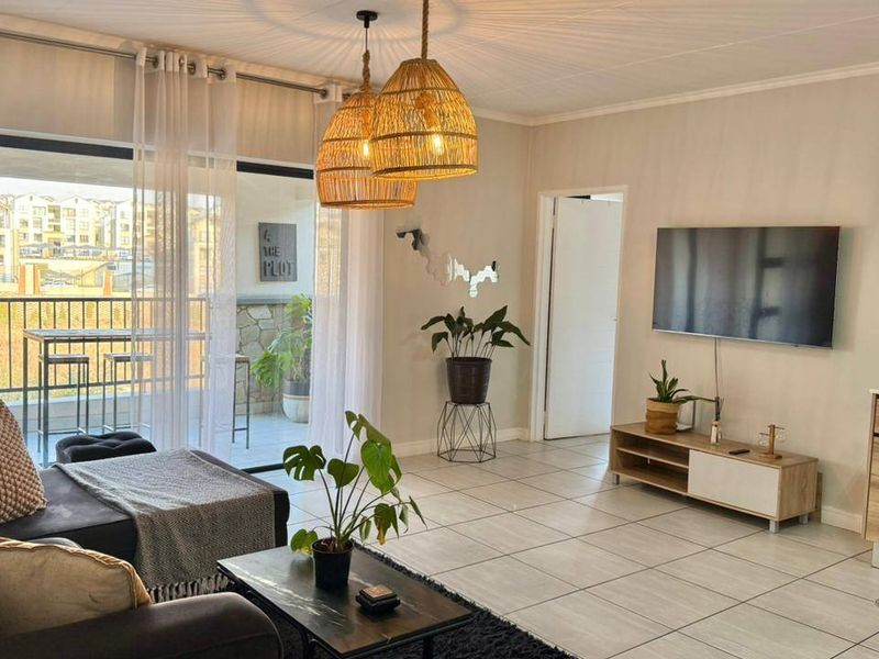 Modern open-plan living area featuring tiled floors, neutral walls, and a seamless transition to a private balcony through large sliding glass doors.