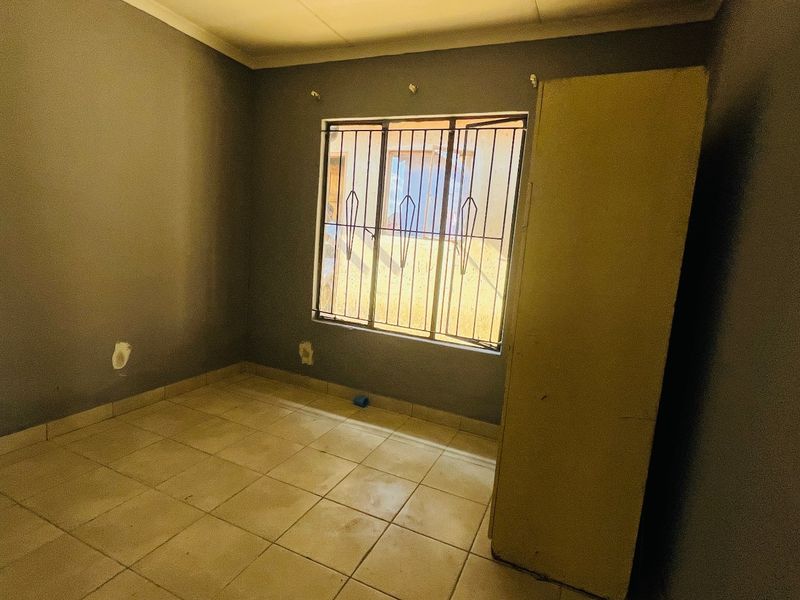 An empty bedroom featuring tiled flooring and a window fitted with security bars, requiring minor cosmetic updates to the walls and flooring.