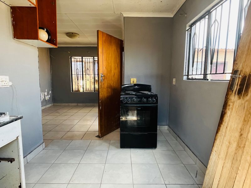 A basic kitchen area featuring tiled floors, a freestanding stove, and security bars on the windows, currently in need of cosmetic updates and repairs.