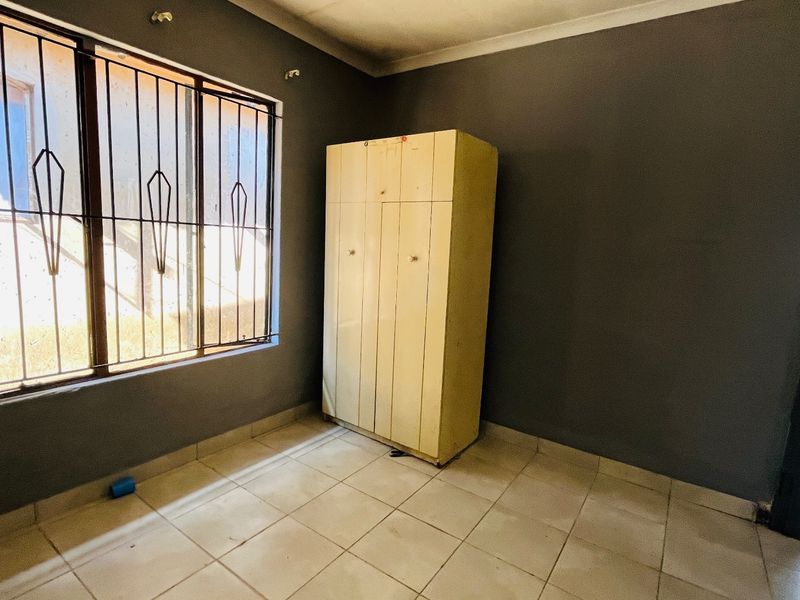 A bedroom featuring tiled flooring, security bars on the window, and a built-in cupboard, requiring some cosmetic attention to the walls and flooring.