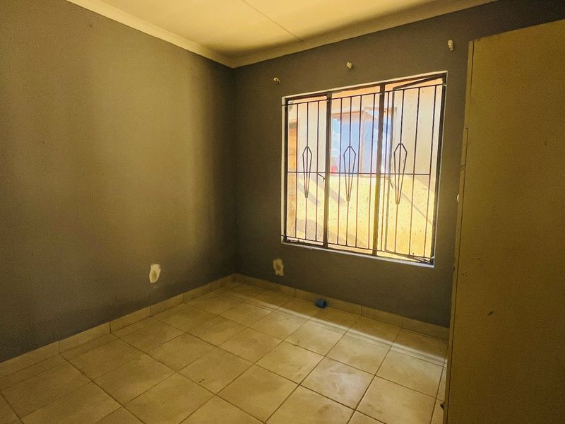 An empty bedroom featuring tiled flooring, security bars on the window, and a built-in cupboard, requiring minor cosmetic updates.