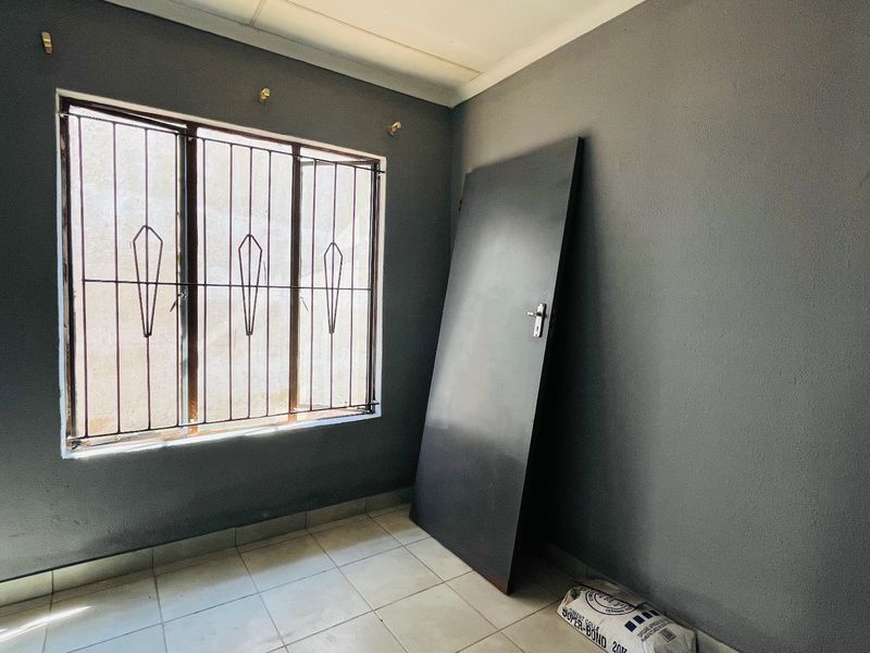 An empty bedroom featuring tiled flooring, security bars on the window, and a detached door leaning against the wall.