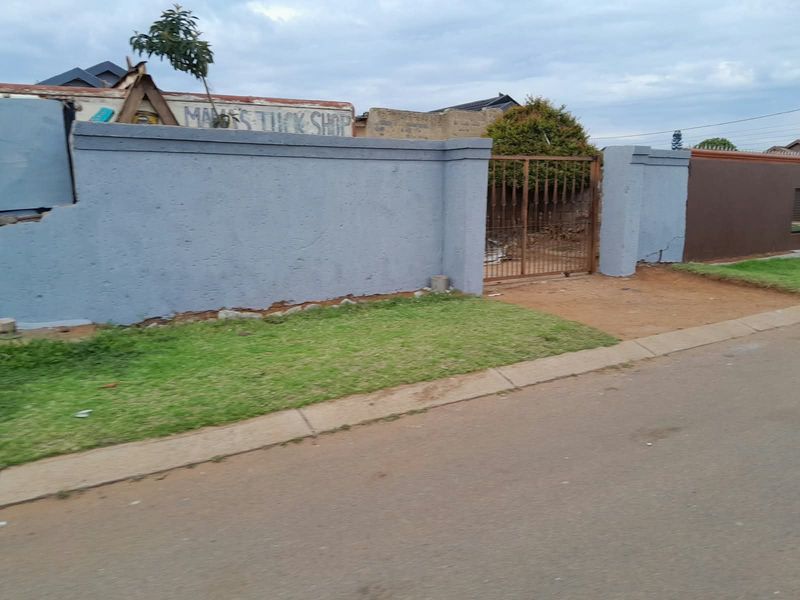 Front view of the property featuring a perimeter wall and metal gate entrance with visible signs of wear and structural cracking.