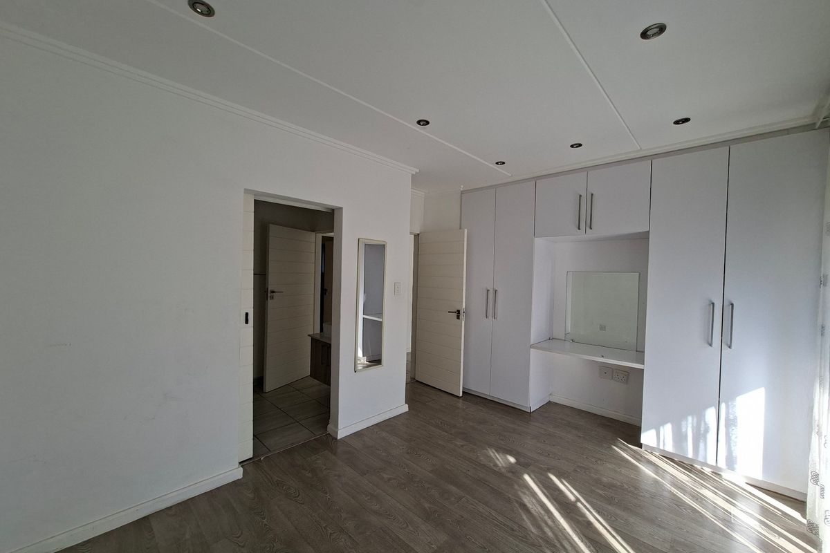 Spacious bedroom featuring modern laminate flooring, extensive built-in cupboards with an integrated vanity station, and recessed ceiling lighting.