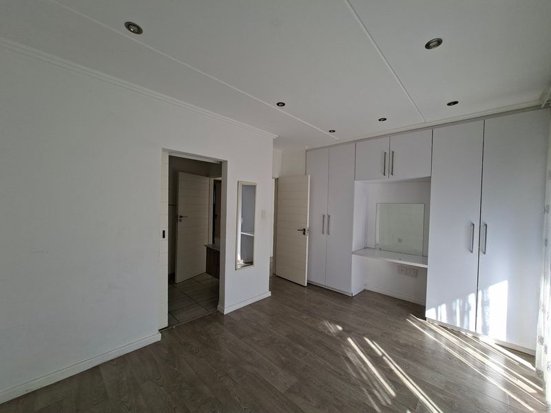 Spacious bedroom featuring modern laminate flooring, extensive built-in cupboards with an integrated vanity station, and recessed ceiling lighting.
