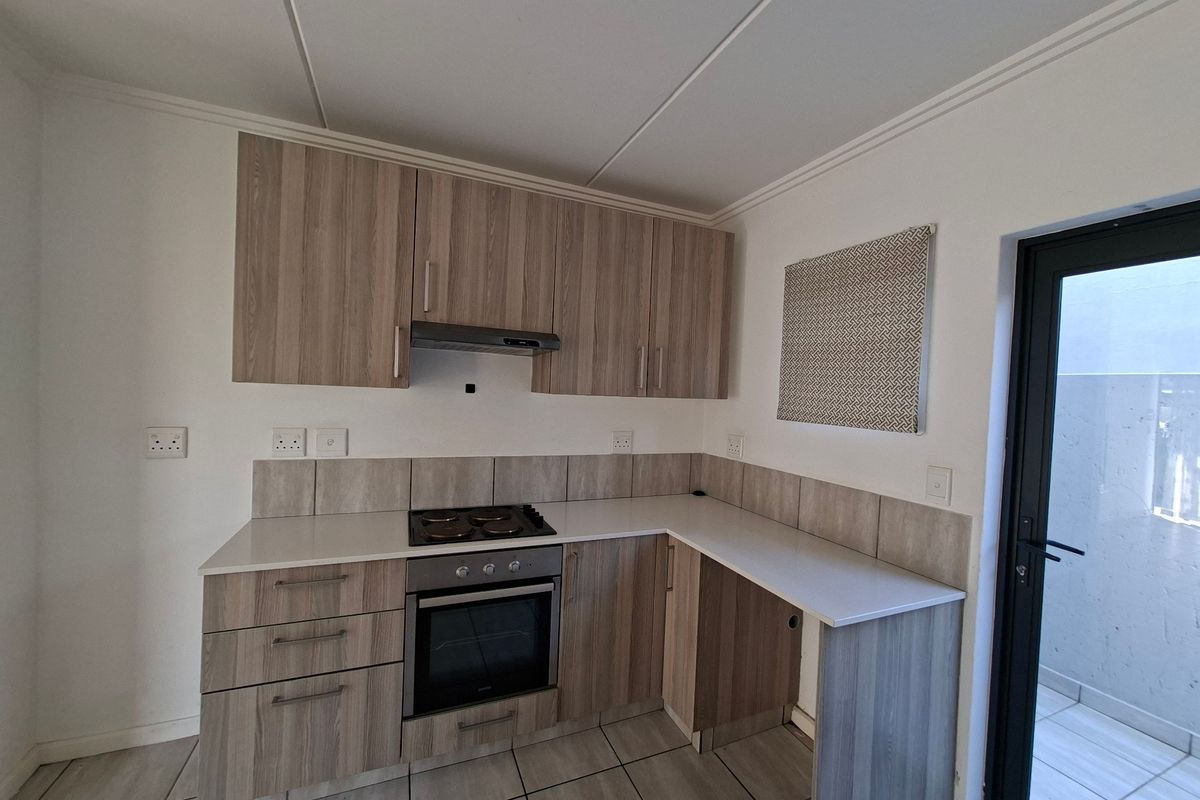 A clean, modern kitchen featuring light wood-grain cabinetry, built-in oven and hob, tiled splashbacks, and direct access to an outdoor area.