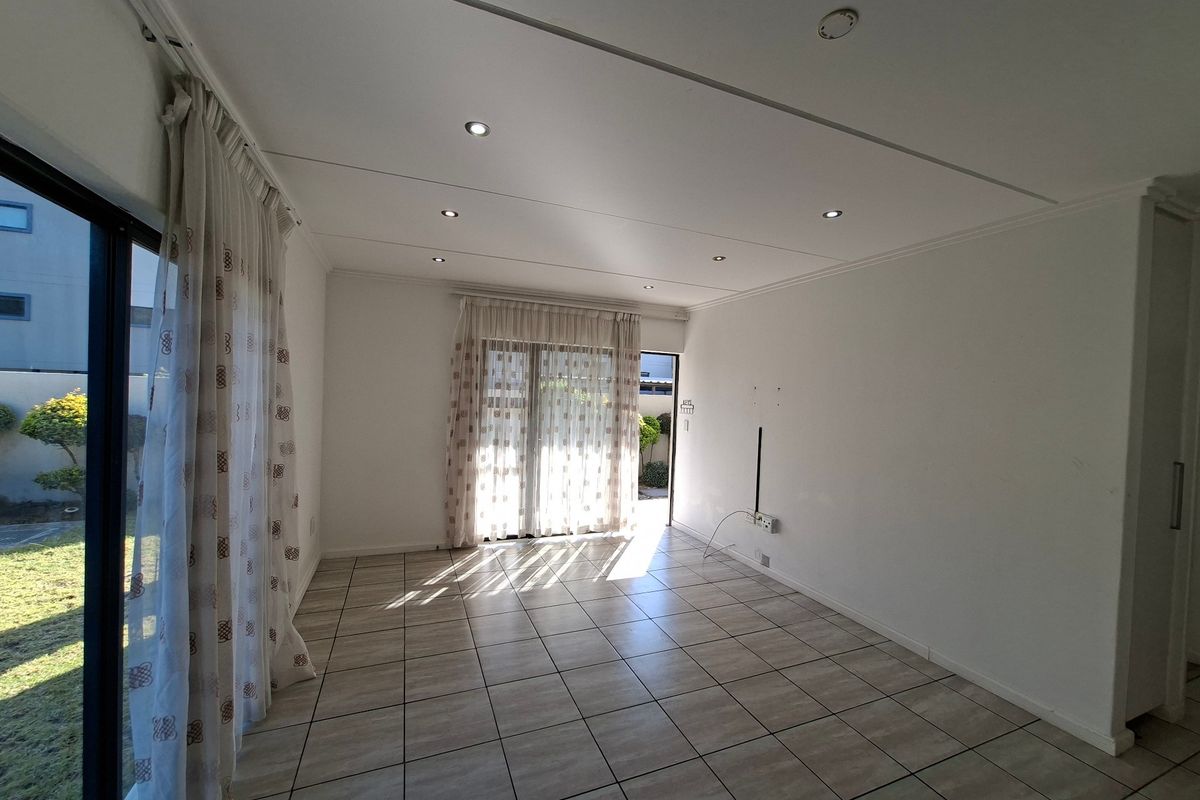 A bright, empty living room featuring tiled flooring, recessed downlights, and large sliding glass doors providing access to the outdoor area.