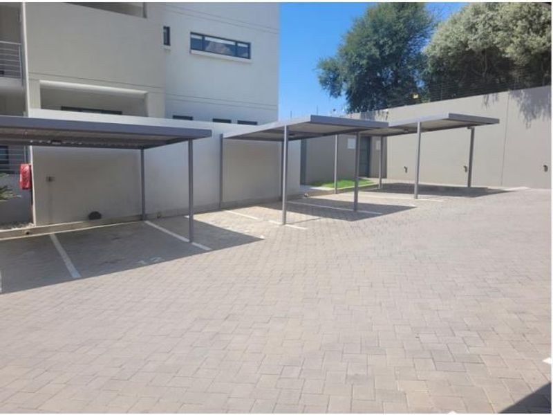 A paved outdoor parking area featuring multiple covered carports and secure perimeter walling.