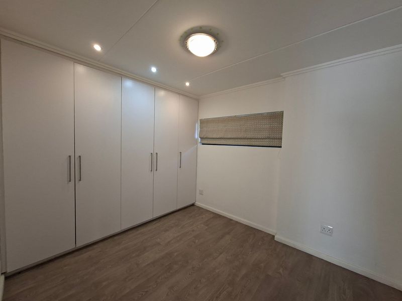 A clean, empty bedroom featuring modern laminate flooring, ample built-in cupboard storage, and recessed lighting.
