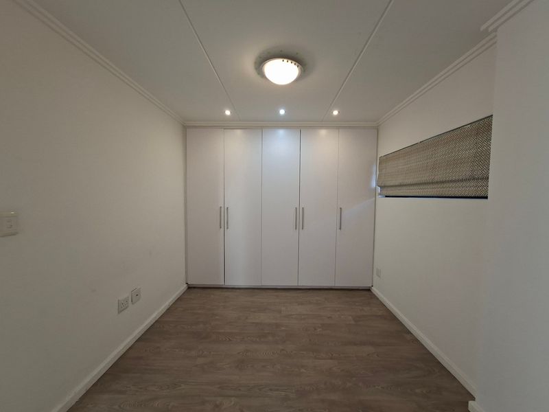 A clean, empty bedroom featuring modern laminate flooring, ample built-in cupboard storage, and neutral finishes, ready for personalization.