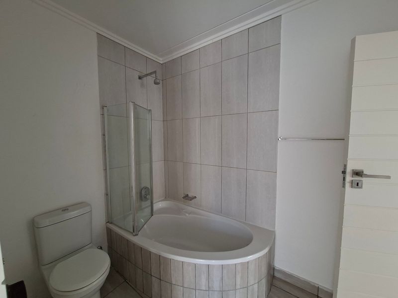 A clean, modern bathroom featuring a built-in bathtub with a glass shower screen, tiled surround, and a standard toilet.