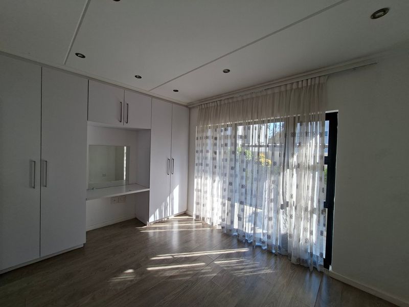 Bright bedroom featuring extensive built-in cupboards with an integrated vanity, modern laminate flooring, and direct access to the outdoors via a sliding glass door.