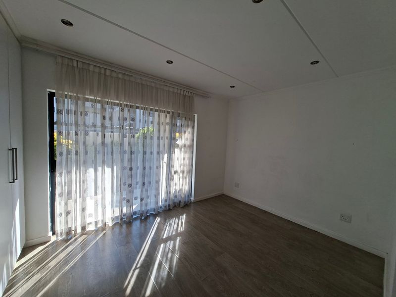 A bright, empty bedroom featuring modern laminate flooring, recessed ceiling lighting, and a large sliding glass door providing access to the exterior.
