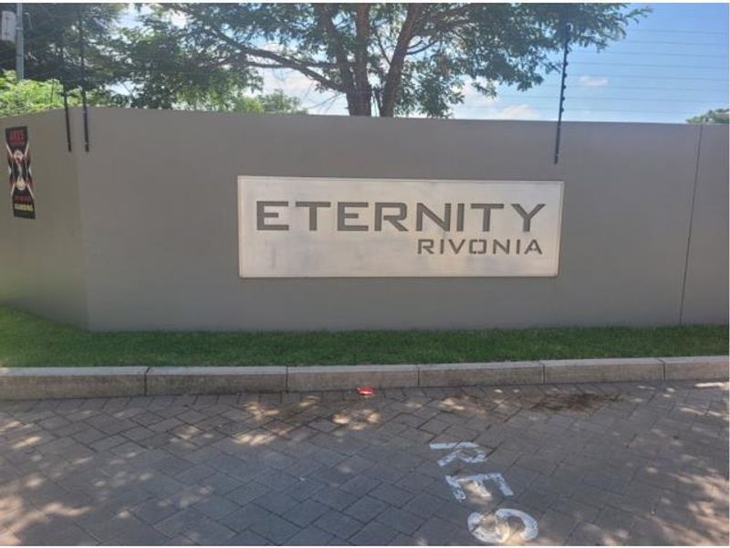 The entrance to the Eternity Rivonia apartment complex, featuring a secure boundary wall with electric fencing and paved driveway access.