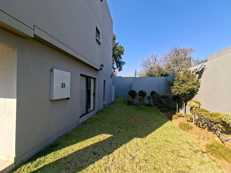 A private rear garden area featuring a well-maintained lawn, boundary walls, and direct access to the apartment via a sliding door.
