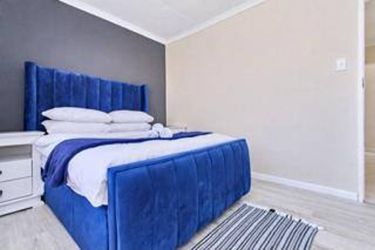 A well-maintained bedroom featuring light-toned laminate flooring and a contrasting dark accent wall with decorative coving.
