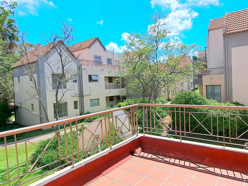 A spacious balcony featuring tiled flooring and a metal balustrade, offering an elevated view of the surrounding apartment complex and landscaped grounds.