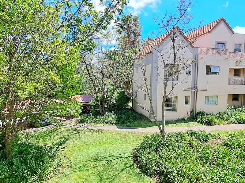 A view of the rear apartment building facade featuring a tiled roof, security bars on windows, and a well-maintained surrounding garden and paved walkway.