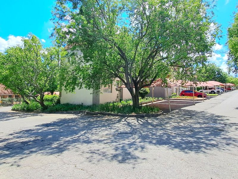 Exterior view of the apartment complex featuring covered parking bays, mature trees, and paved driveway access.