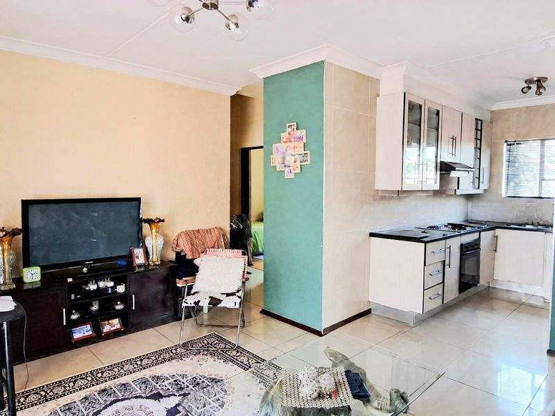 Open-plan living area featuring a functional kitchen with built-in cabinetry, oven, and hob, seamlessly connected to the main living space with tiled flooring.