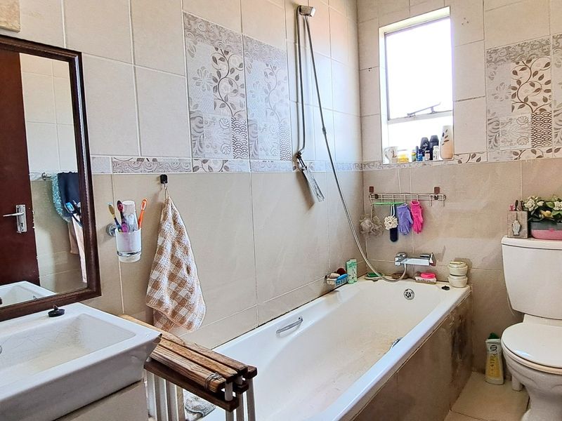 A functional bathroom featuring a bathtub with shower mixer, toilet, and vanity basin with tiled walls and flooring.