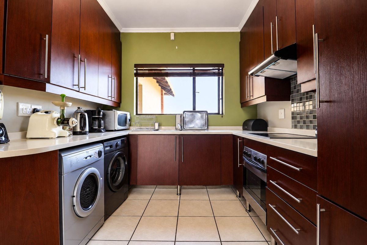 A functional kitchen featuring dark wood cabinetry, stone countertops, tiled flooring, and integrated appliances including an oven, hob, and extractor fan.