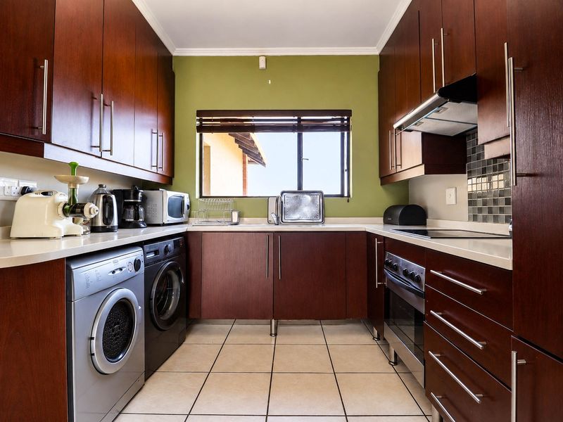 A functional kitchen featuring dark wood cabinetry, stone countertops, tiled flooring, and integrated appliances including an oven, hob, and extractor fan.