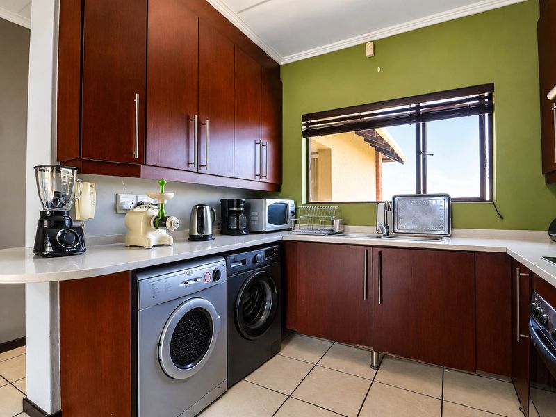A functional kitchen featuring dark wood cabinetry, stone countertops, integrated appliances, and tiled flooring with a window providing natural light.