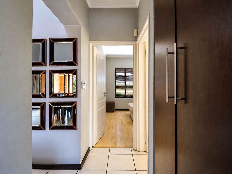 A well-maintained hallway featuring tiled flooring, a built-in cupboard, and an archway leading into a bedroom with wooden flooring.