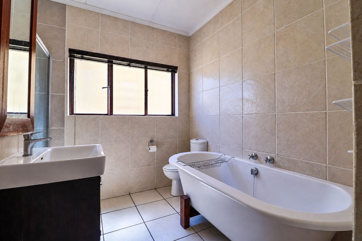 A well-maintained bathroom featuring a freestanding bathtub, wall-mounted basin, toilet, and neutral floor-to-ceiling tiling.