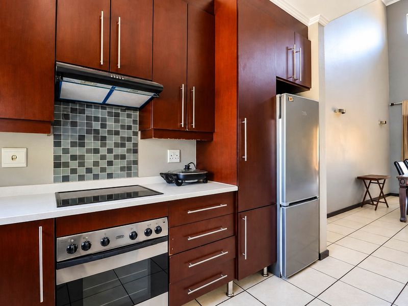 A well-maintained kitchen featuring dark wood cabinetry, stone countertops, a mosaic tile backsplash, and integrated appliances, flowing into an open-plan dining area.
