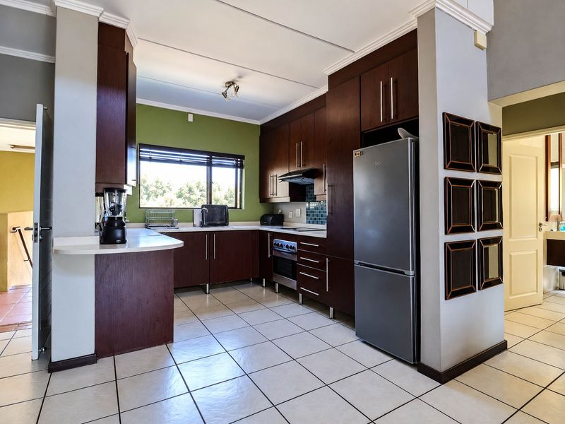 A functional kitchen featuring dark wood cabinetry, laminate countertops, tiled backsplash, and built-in oven with extractor fan, complemented by tiled flooring.