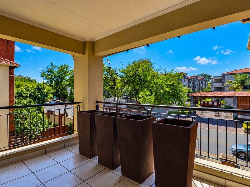 A covered balcony featuring tiled flooring and a metal balustrade, offering an elevated view of the surrounding residential complex and street.