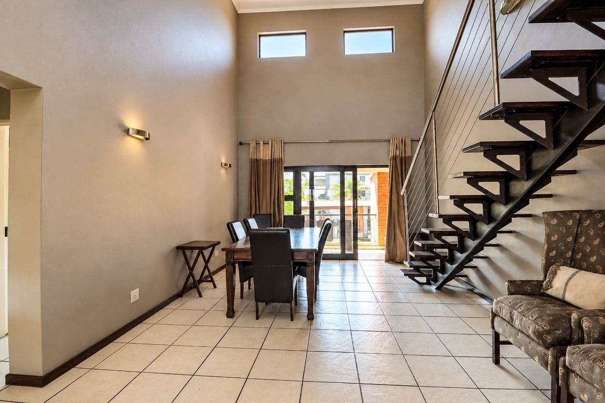 Spacious living area featuring high ceilings, tiled flooring, a modern staircase with stainless steel balustrades, and access to an outdoor balcony.