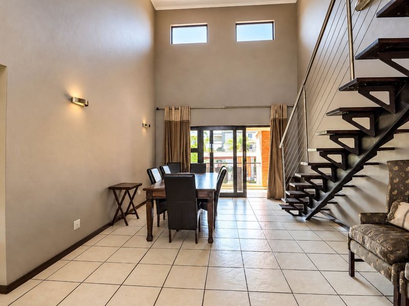 Spacious living area featuring high ceilings, tiled flooring, a modern staircase with stainless steel balustrades, and access to an outdoor balcony.