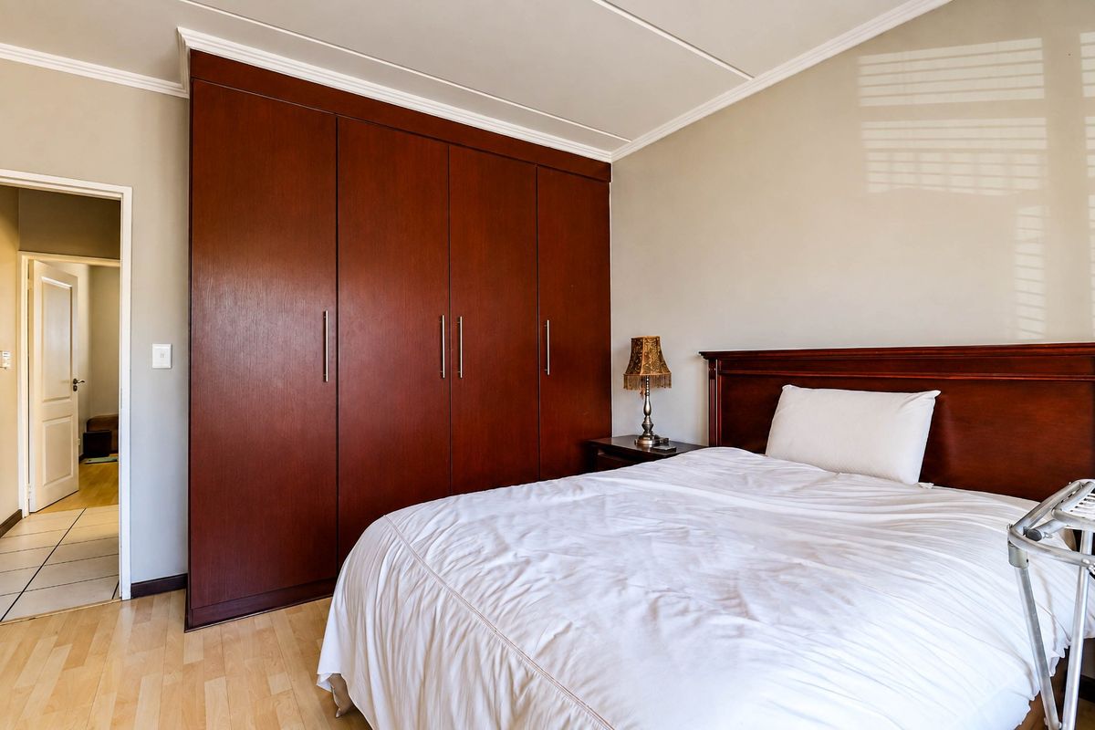 A well-maintained bedroom featuring dark wood built-in cupboards, light laminate flooring, and classic crown molding details.
