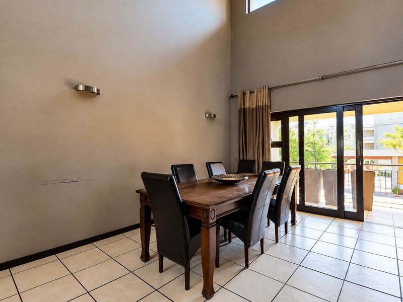 Spacious dining area featuring double volume ceilings, tiled flooring, and large sliding glass doors providing access to an outdoor balcony.