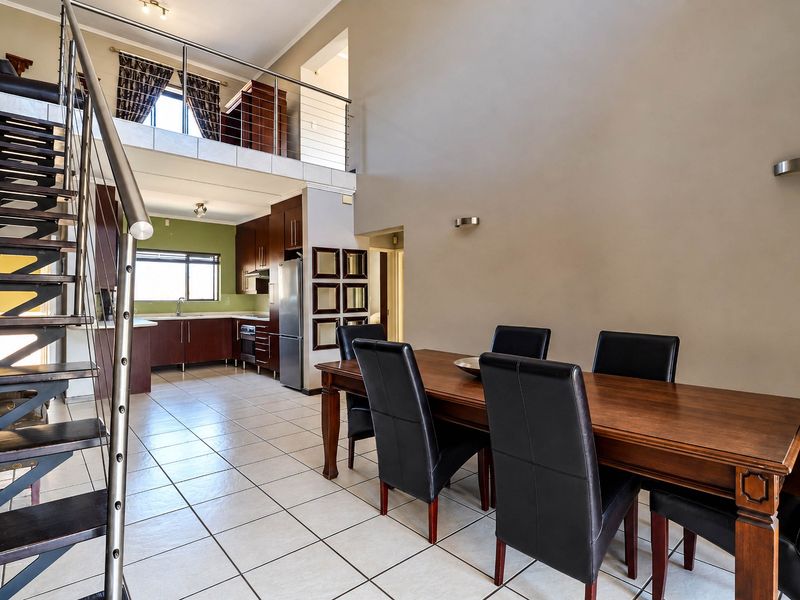 Spacious open-plan living area featuring a double-volume ceiling, tiled flooring, a modern staircase with stainless steel balustrades, and an integrated kitchen.