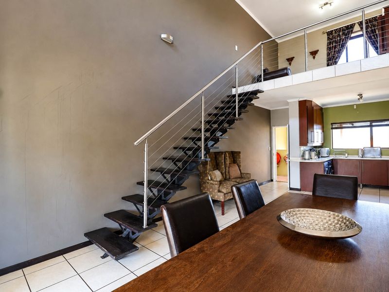 Open plan living area featuring a modern staircase with stainless steel balustrade, mezzanine level, and an integrated kitchen with dark wood cabinetry.