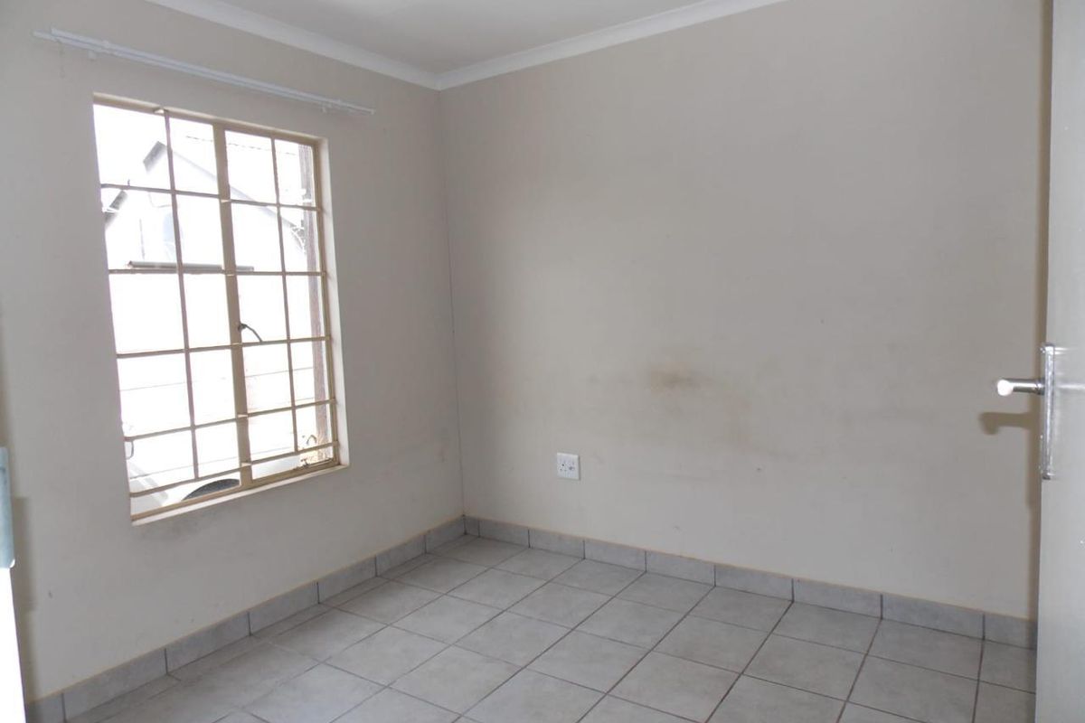 An empty bedroom featuring tiled flooring, a window with security bars, and neutral wall finishes, ready for personalization.
