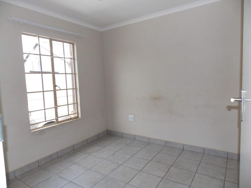 An empty bedroom featuring tiled flooring, a window with security bars, and neutral wall finishes, ready for personalization.