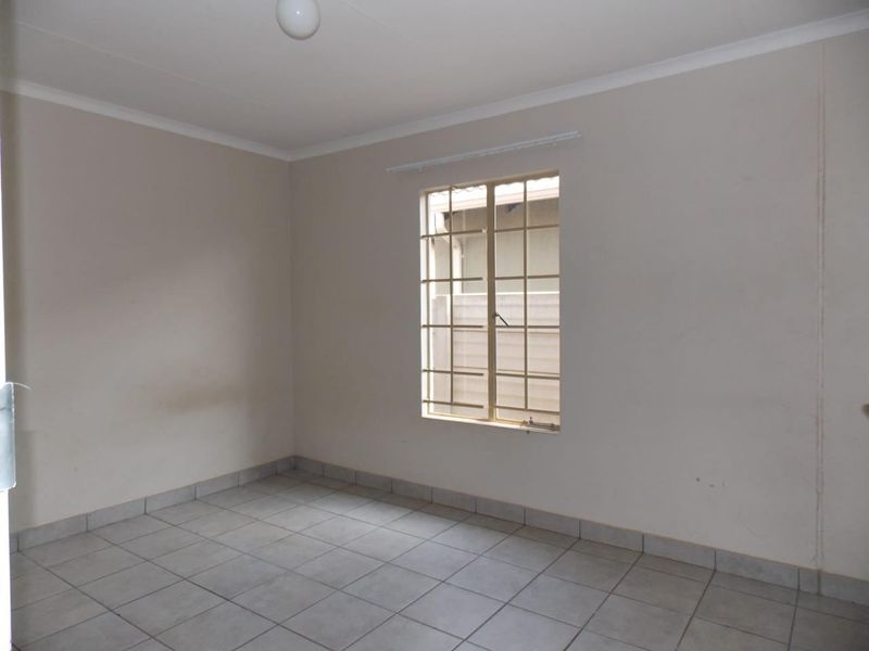 An empty bedroom featuring neutral wall paint, tiled flooring, and a window fitted with security bars.