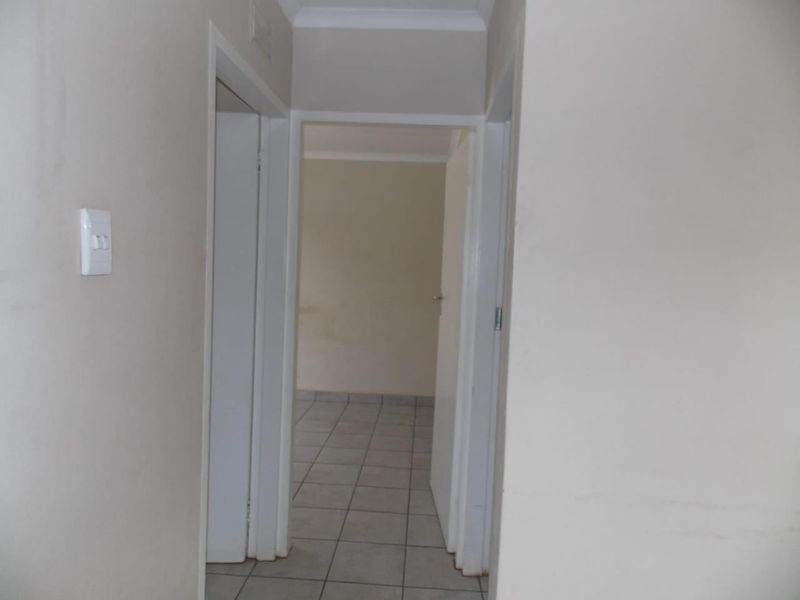A simple, empty hallway with neutral wall paint and tiled flooring, providing access to adjacent rooms.