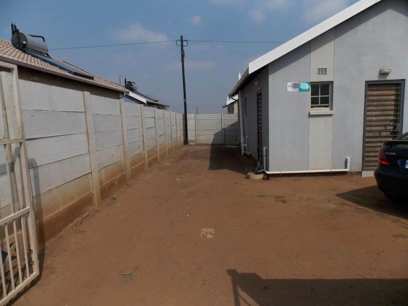 Rear exterior view showing a side yard with a precast concrete boundary wall, solar water heater, and unpaved ground area.