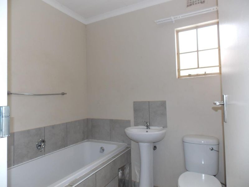 A functional bathroom featuring a pedestal washbasin, built-in bathtub, and toilet with neutral wall finishes and tiled splashbacks.