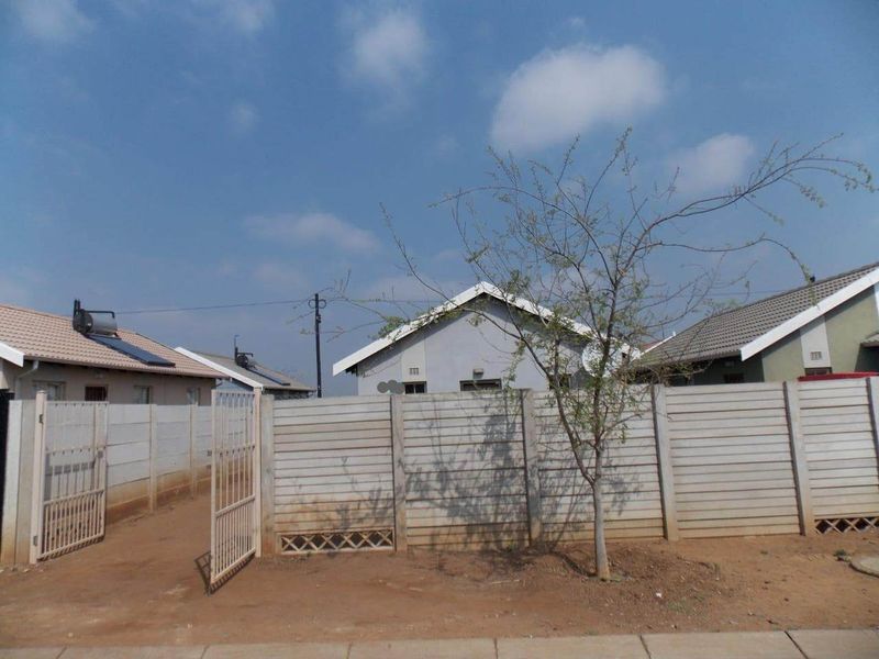 Front view of a residential property featuring a precast concrete boundary wall, metal pedestrian gate, and tiled roof with a solar water heater.