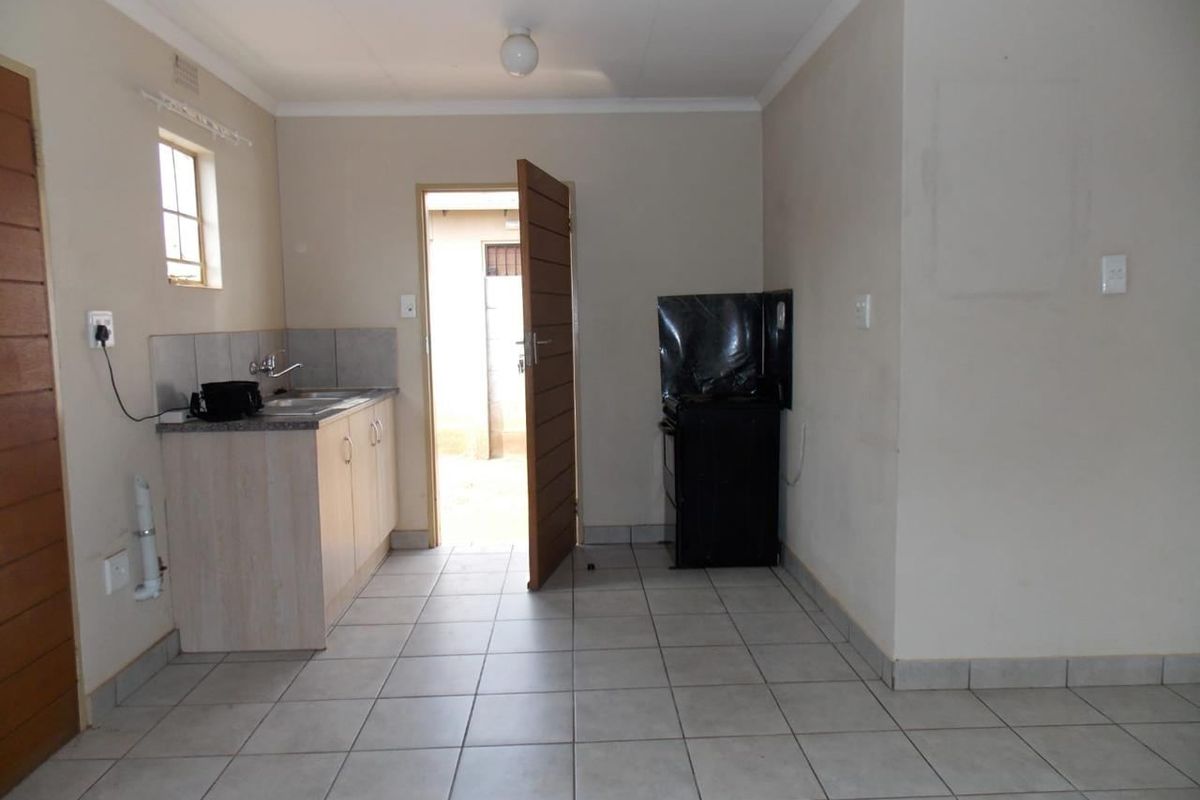 A functional, compact kitchen featuring tiled flooring, basic cabinetry with a stainless steel sink, and a freestanding stove, with direct access to the exterior.
