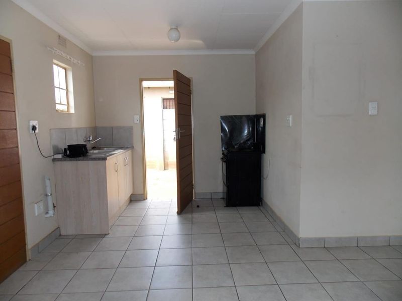 A functional, compact kitchen featuring tiled flooring, basic cabinetry with a stainless steel sink, and a freestanding stove, with direct access to the exterior.
